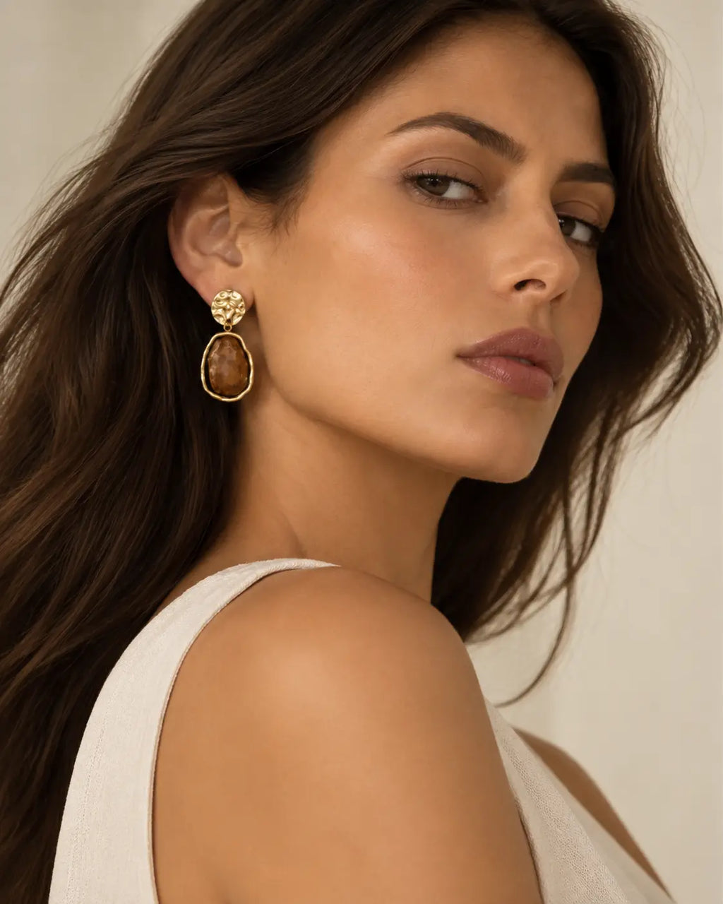 Faceted brown drop earring visible in an over-the-shoulder portrait.