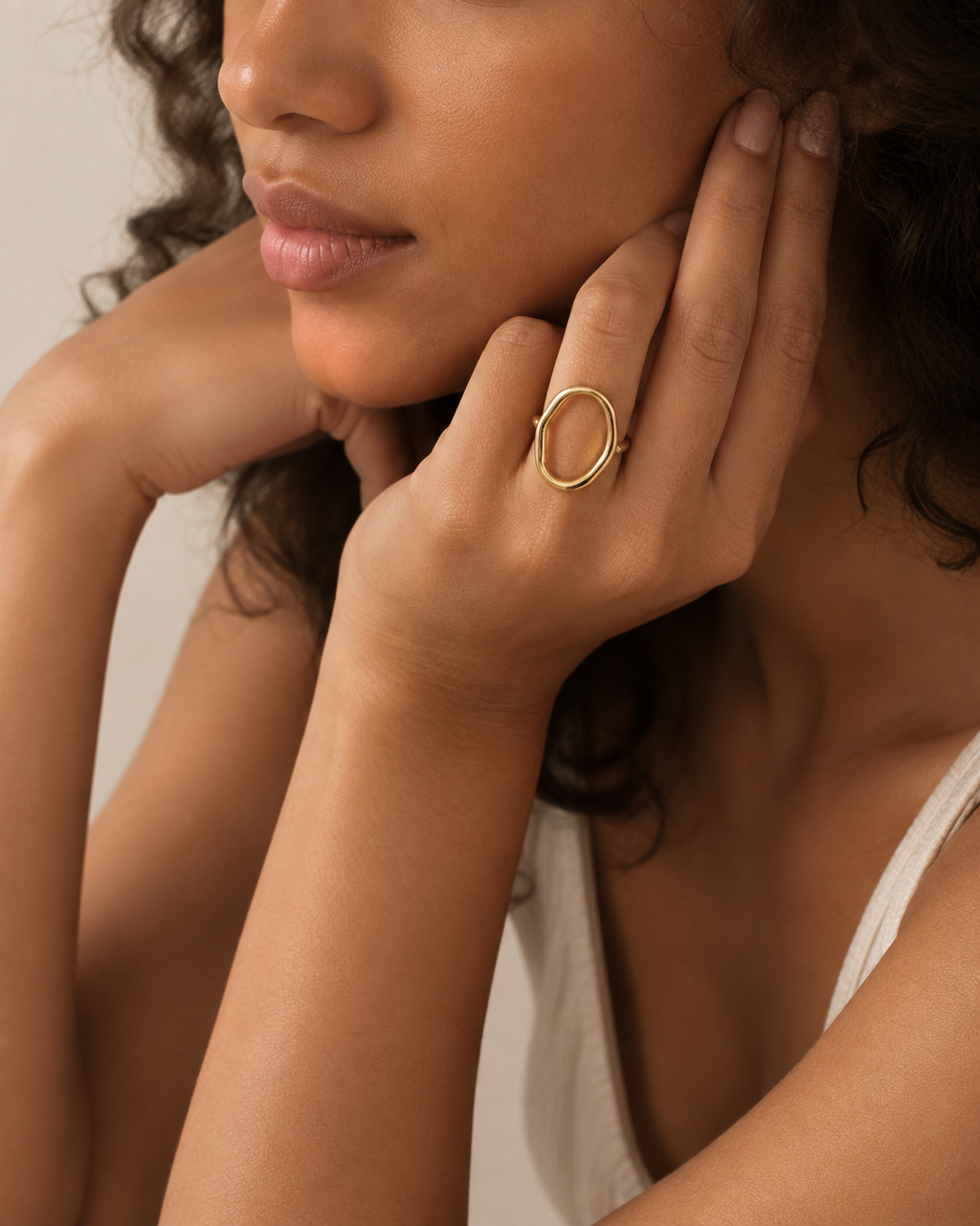 Gold-tone open ring with a tall hollow oval outline, worn with the head resting against the hand.