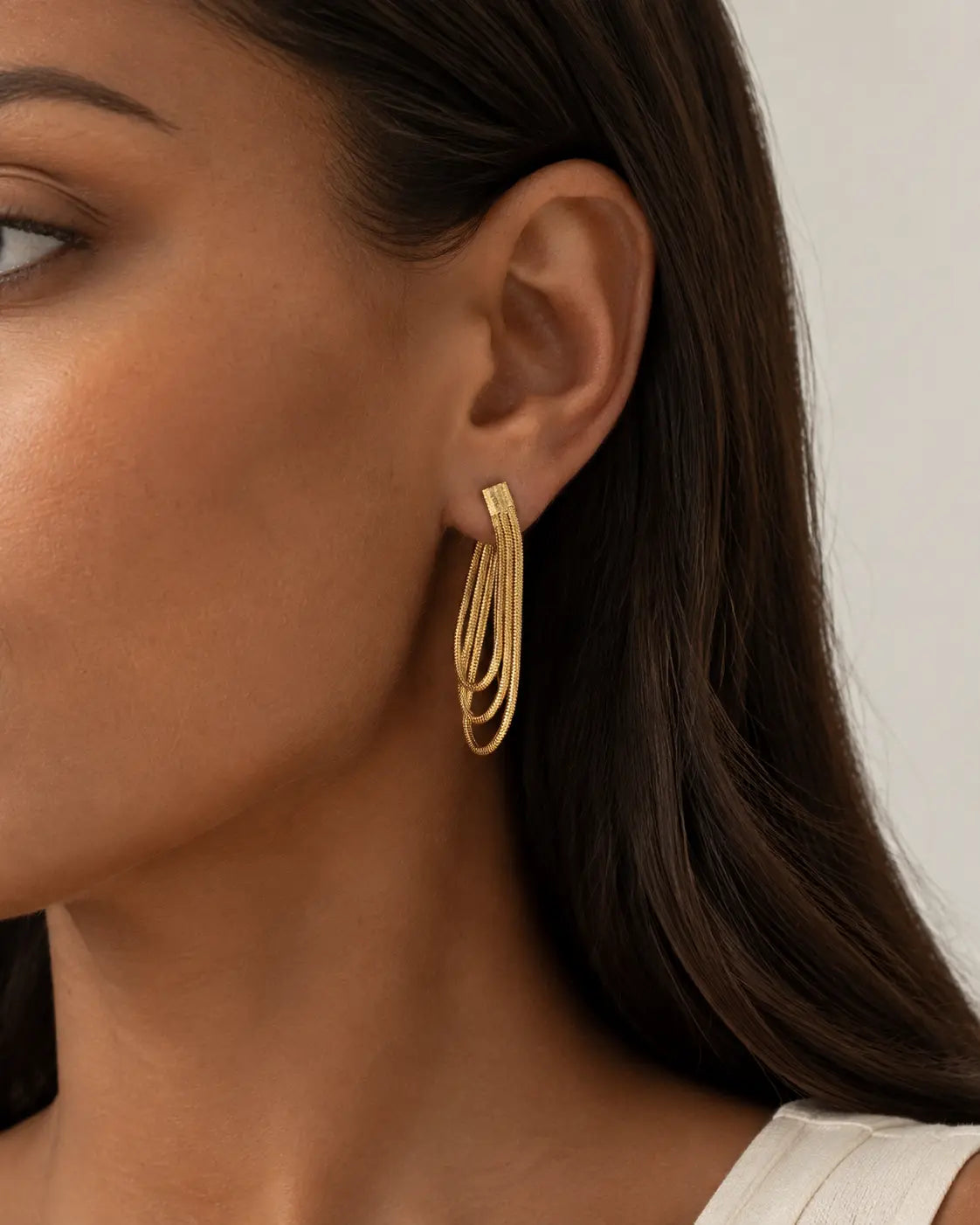 Close-up of a gold-tone looped-chain drop earring on the ear.