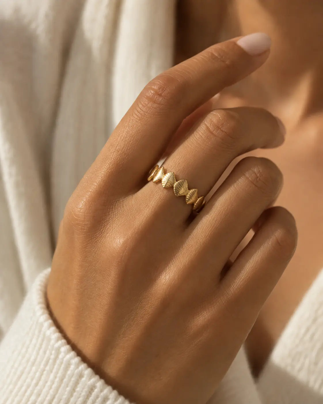 Gold-tone band ring with textured rhombus-shaped motifs, closer view of the textured motifs on a finger.