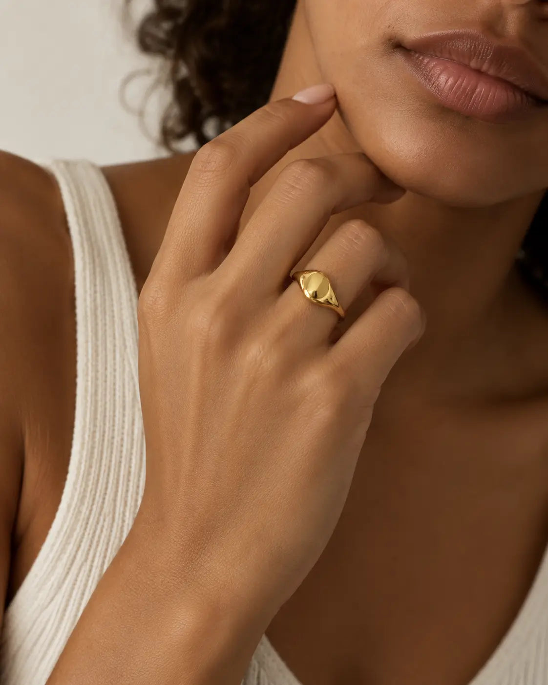Gold-tone ring with an asymmetric domed front, worn on a hand near the chin.