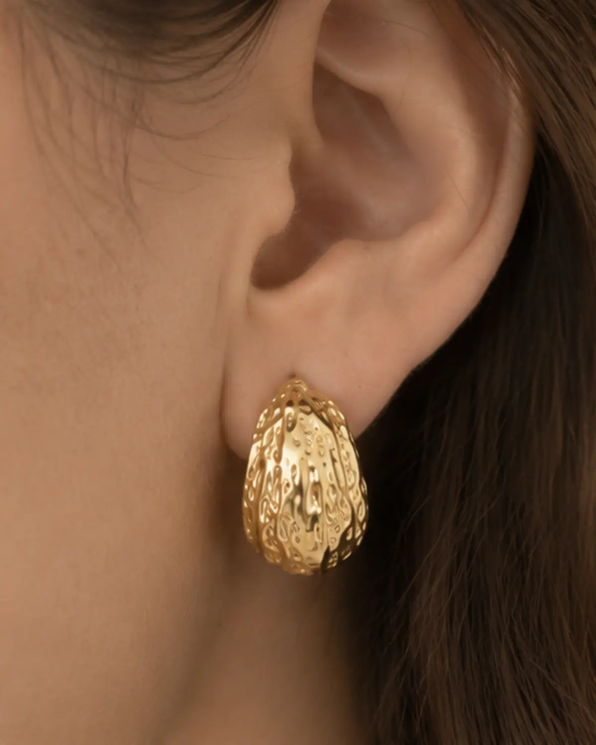 Close-up of a textured gold-tone hoop earring on the ear.
