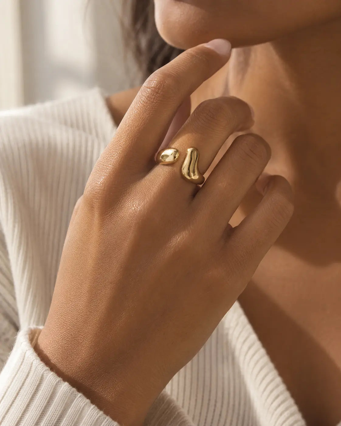 Gold-tone bypass ring with two rounded drop-shaped ends, worn on a raised hand.