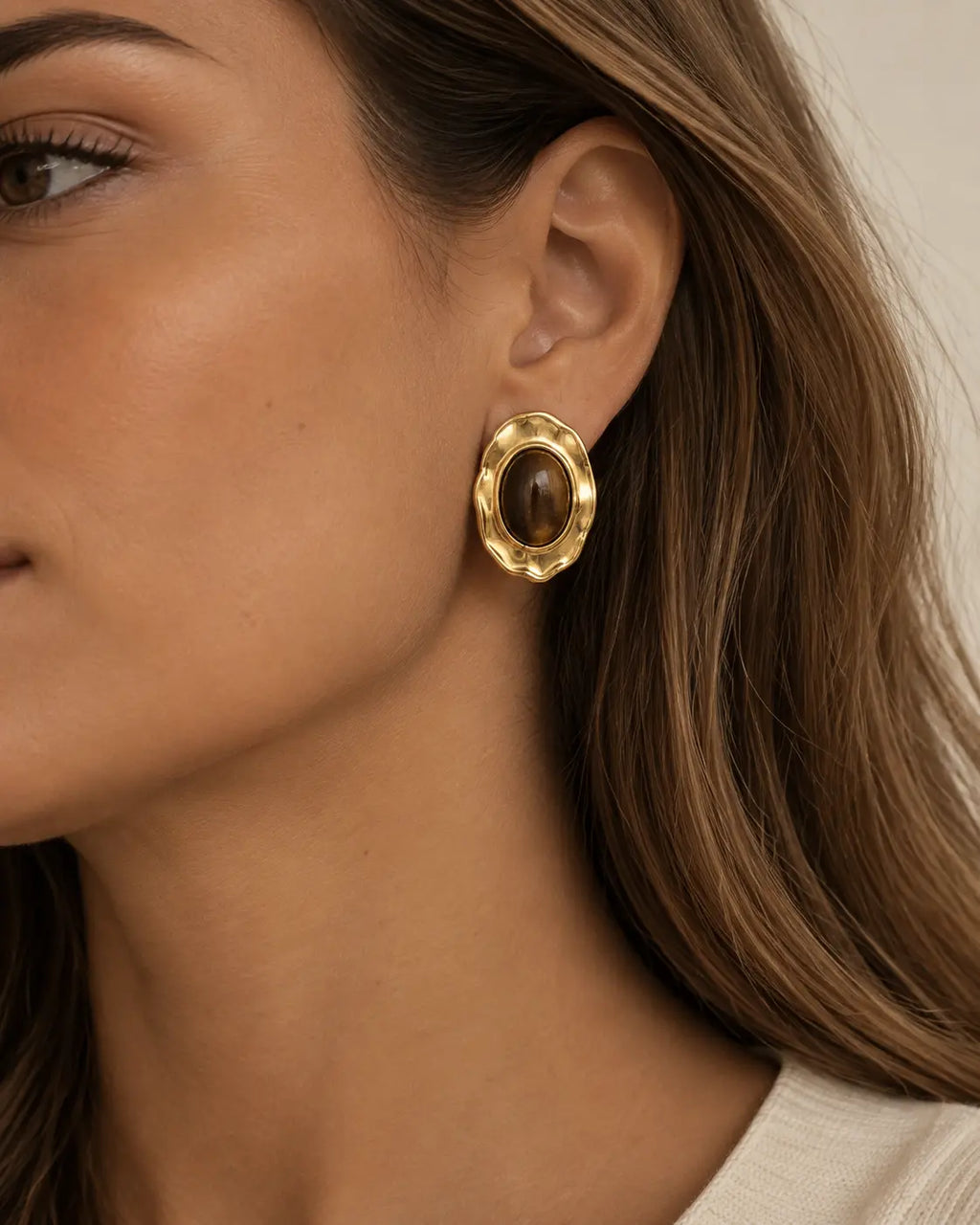 Close-up of a brown oval stud in a hammered gold-tone frame.