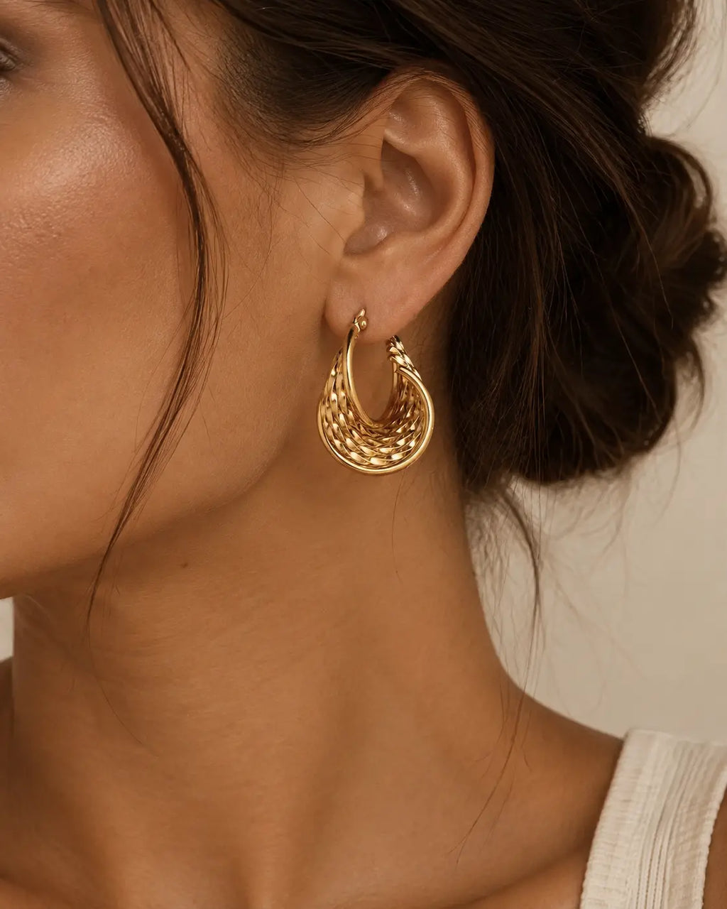 Close-up of a woven gold-tone oval hoop on the ear.