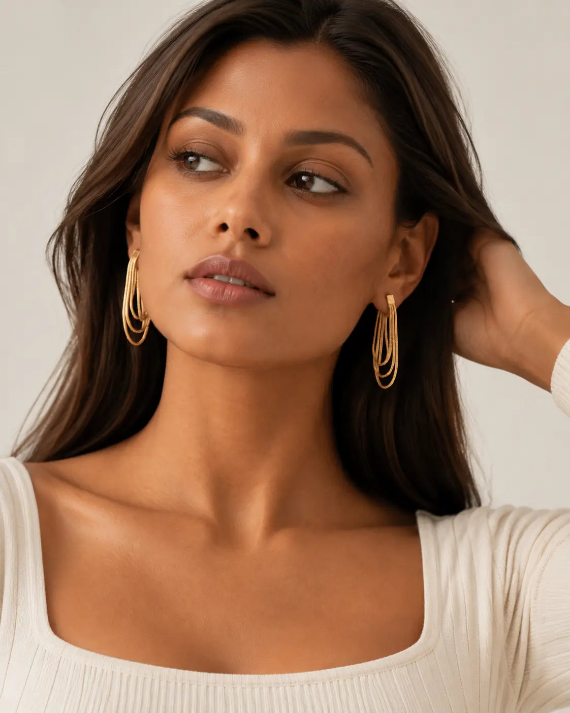 Gold-tone looped-chain earrings worn with a hand beside the hair.