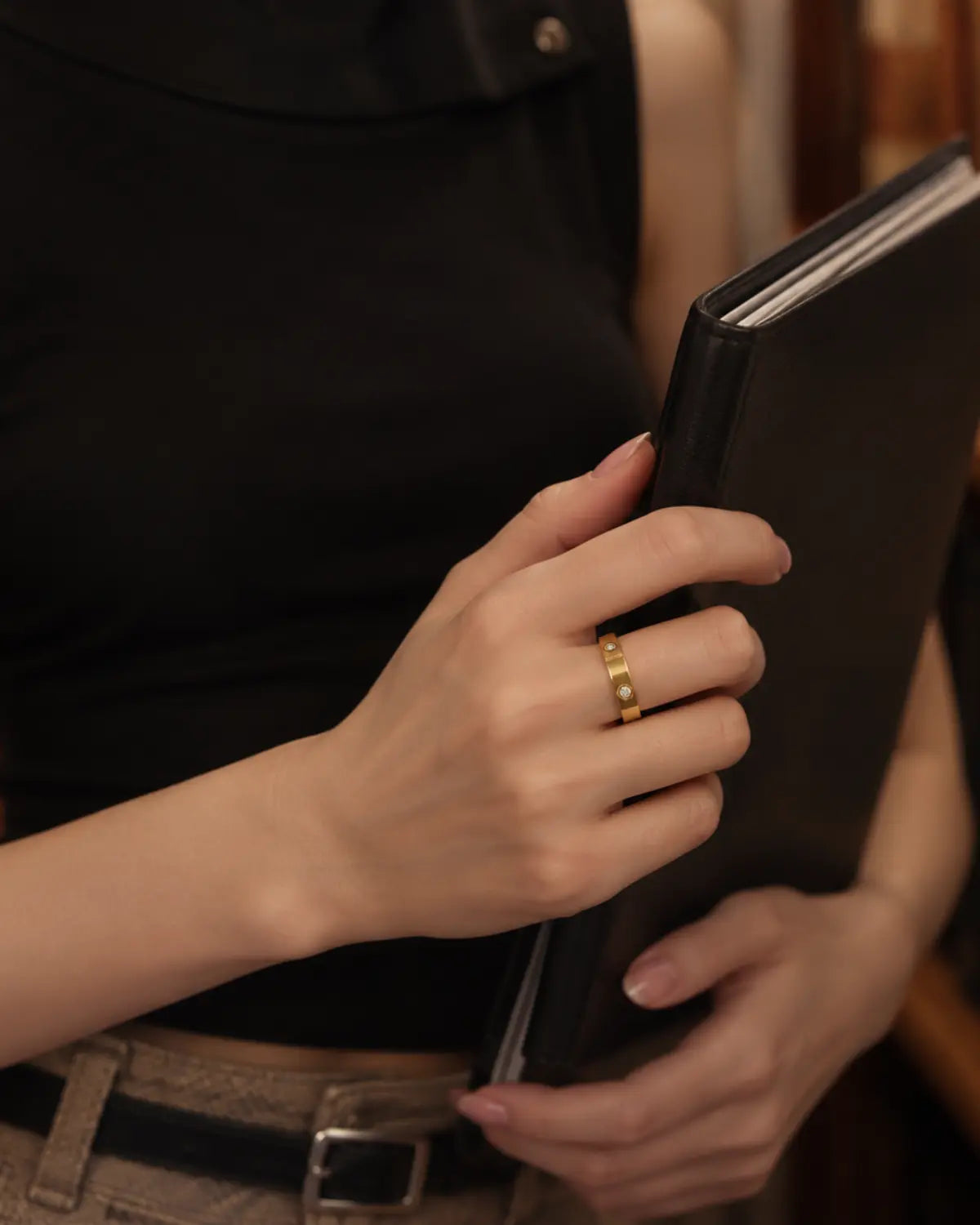 Gold-tone band ring with spaced round bezel-set stone accents, worn on a hand holding a black clutch.