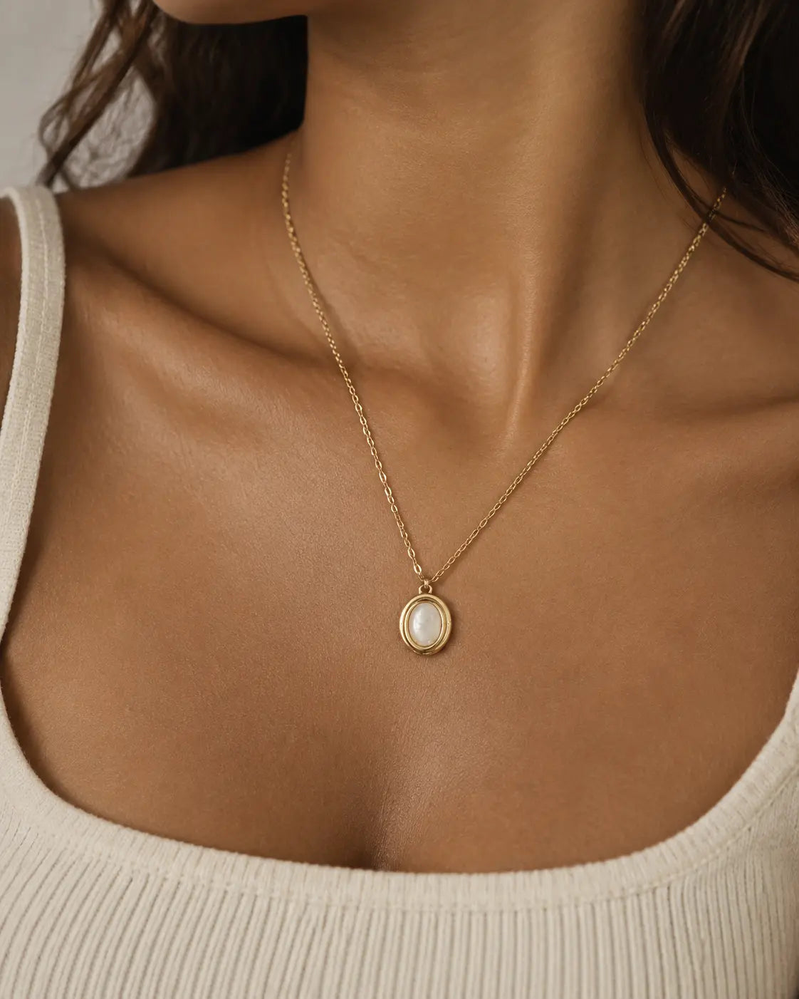 Gold-tone necklace with a white oval accent in a double-rimmed pendant, worn with a white square-neck top.