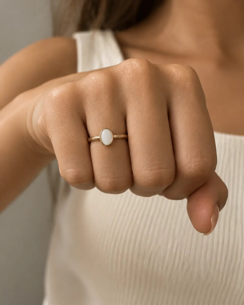 Slim gold-tone ring with a white oval bezel accent, worn on a loosely closed hand.