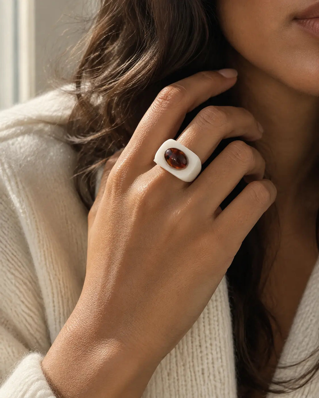 White ring with a contrasting brown oval accent, worn on a hand near the face.