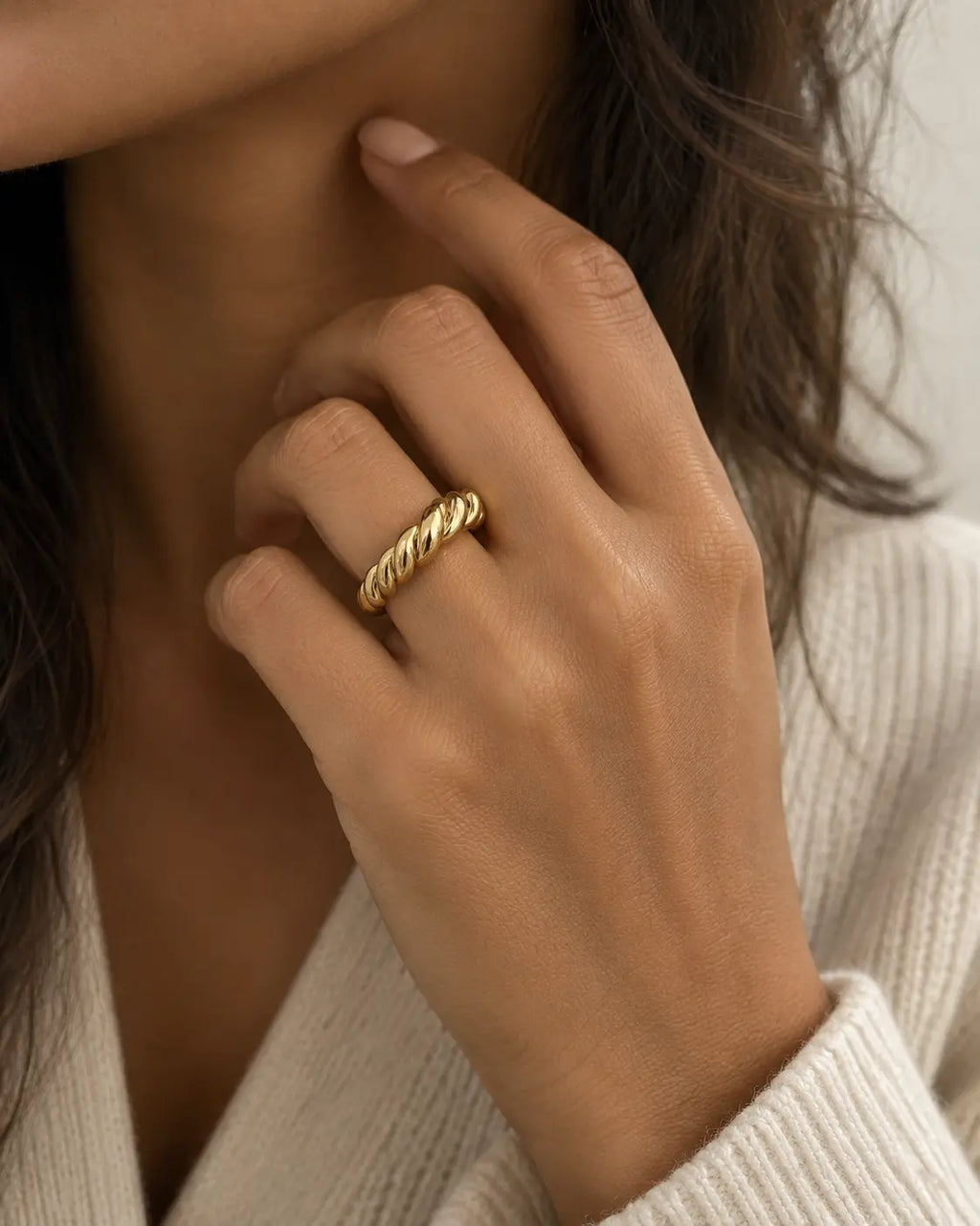 Gold-tone open band ring with a cable-twist pattern, worn on a hand near the chin.