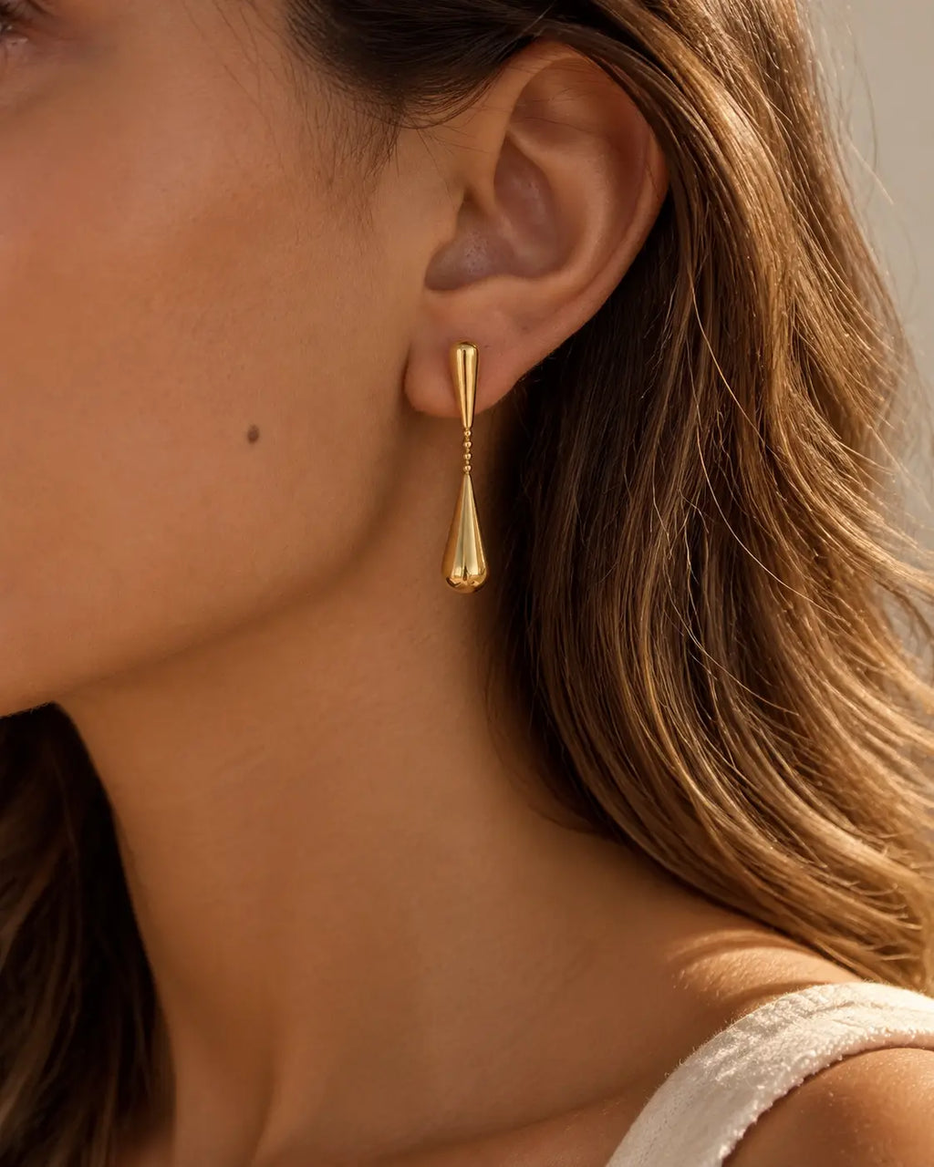 Close-up of a linked gold-tone teardrop earring on the ear.