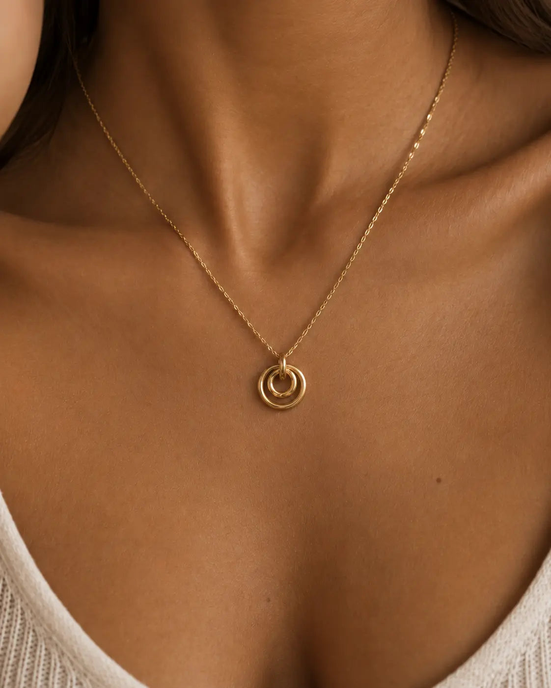 Gold-tone necklace with concentric circle pendants, close-up worn with a white top.
