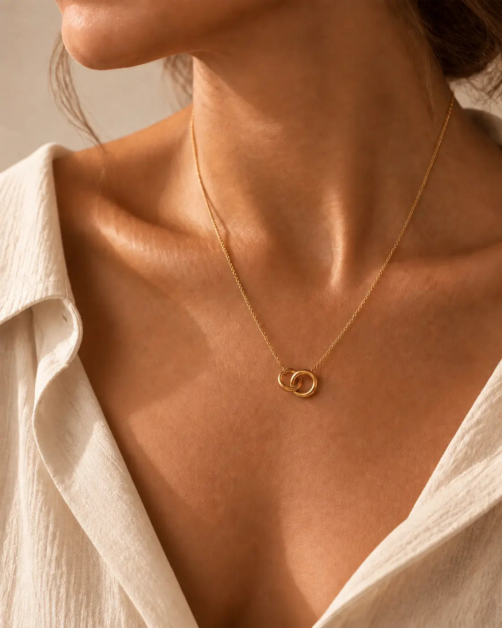 Gold-tone necklace with two interlocking circle pendants, worn inside an open white collar.