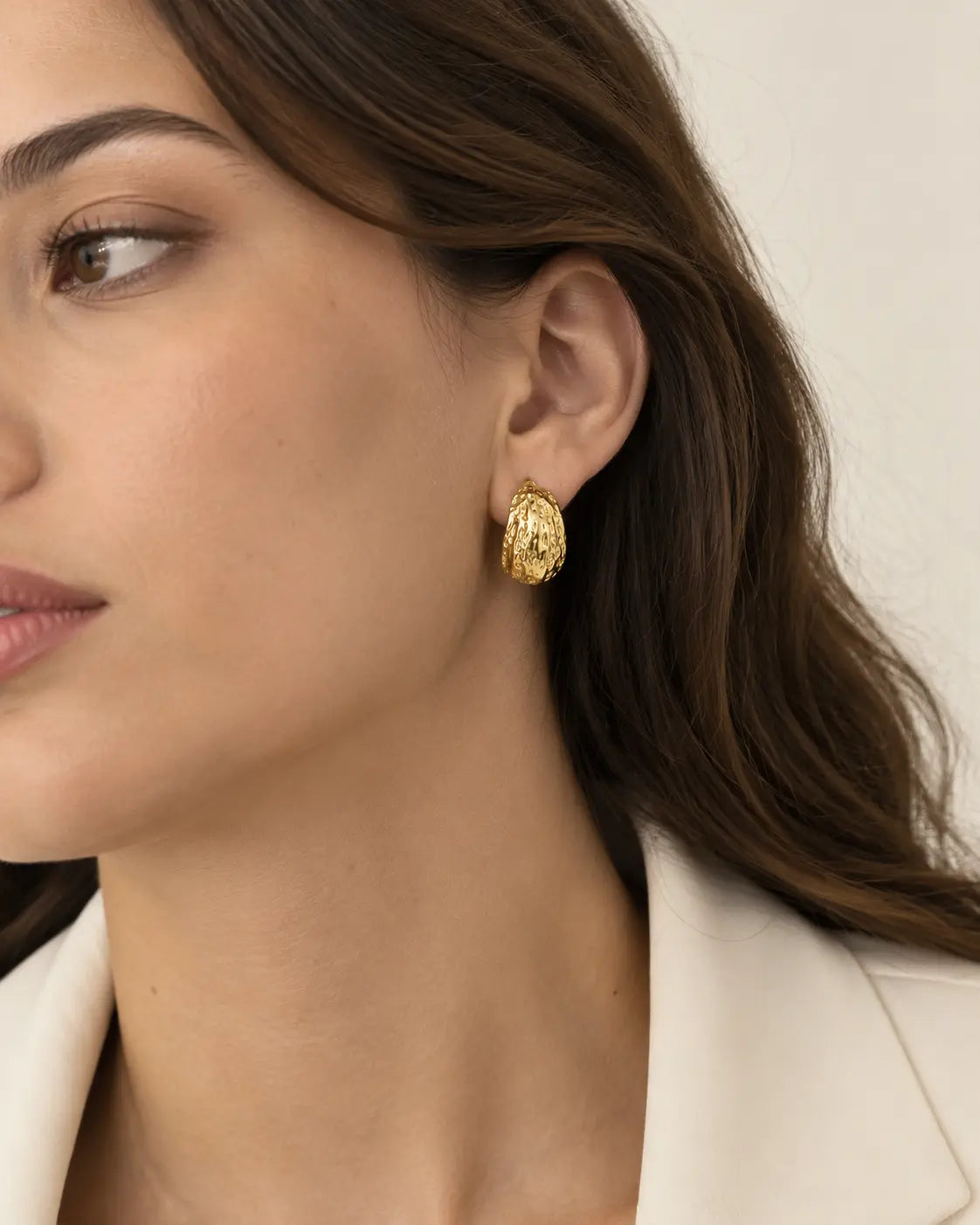 Textured gold-tone hoop earring worn beside a white jacket.