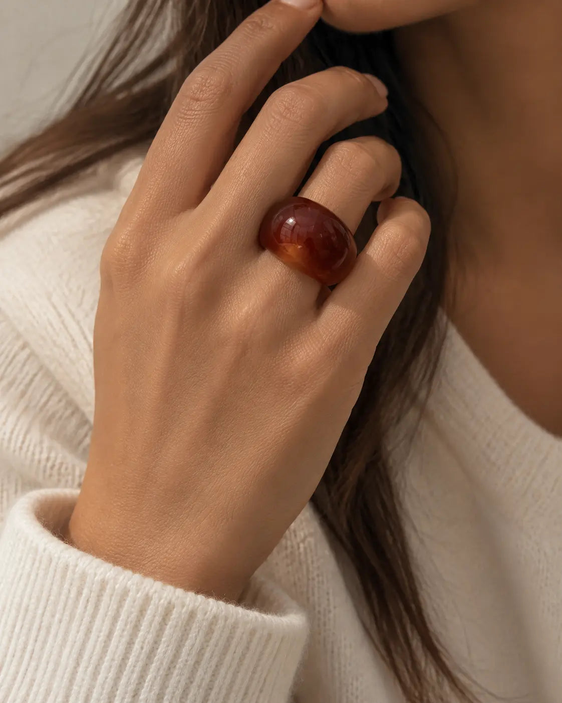 Brown marbled dome ring, worn on a hand near the chin.