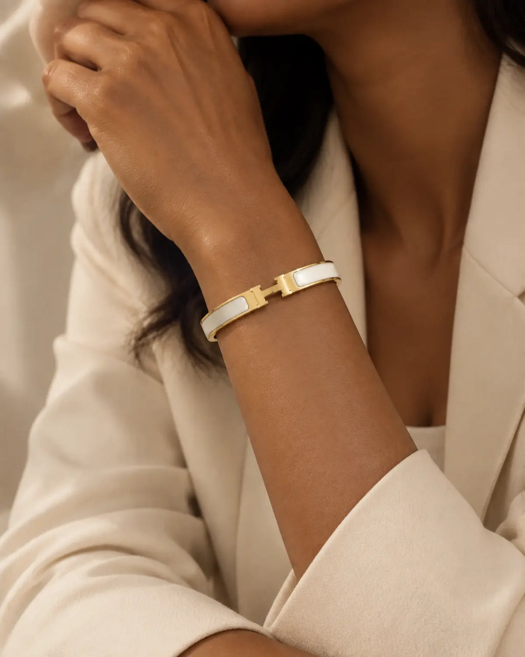 White enamel bangle with gold-tone edges and an H-shaped clasp, worn on a wrist near the face.