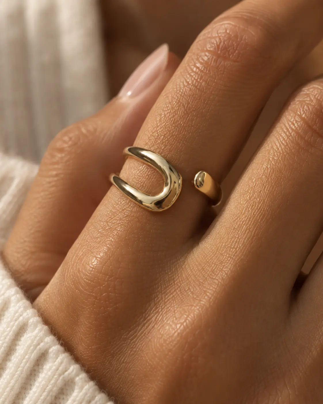 Gold-tone bypass ring with an open loop and tapered end, close-up on a finger.