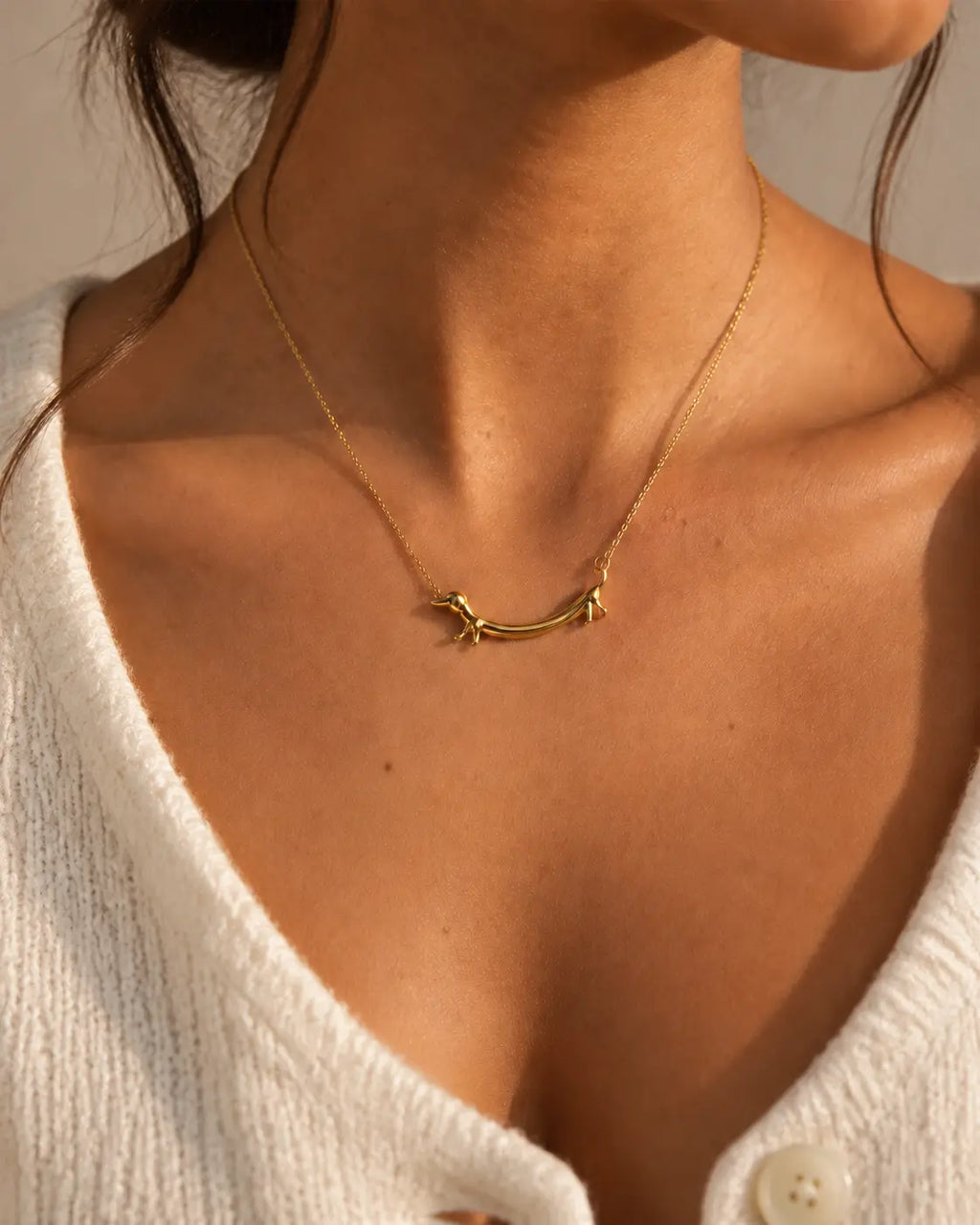 Gold-tone necklace with a dachshund-shaped pendant, worn with a light knitted V-neck top.