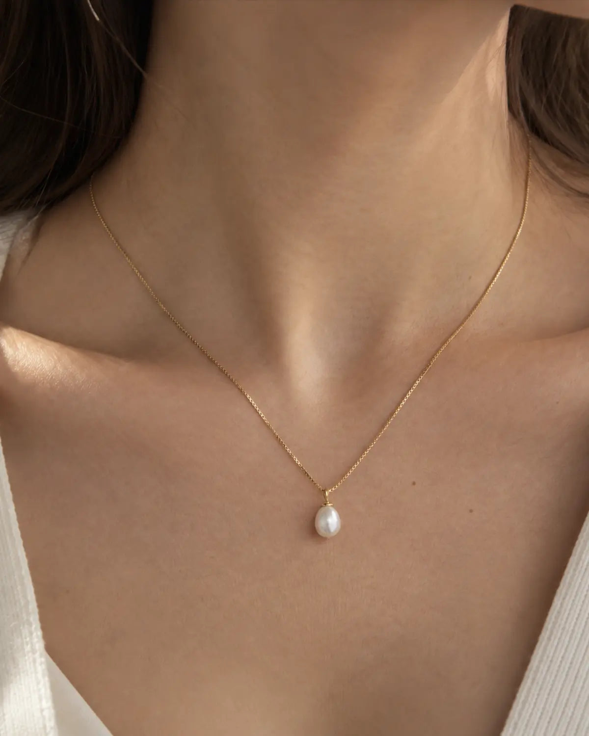 Gold-tone necklace with a white drop pendant, worn with a white V-neck top.