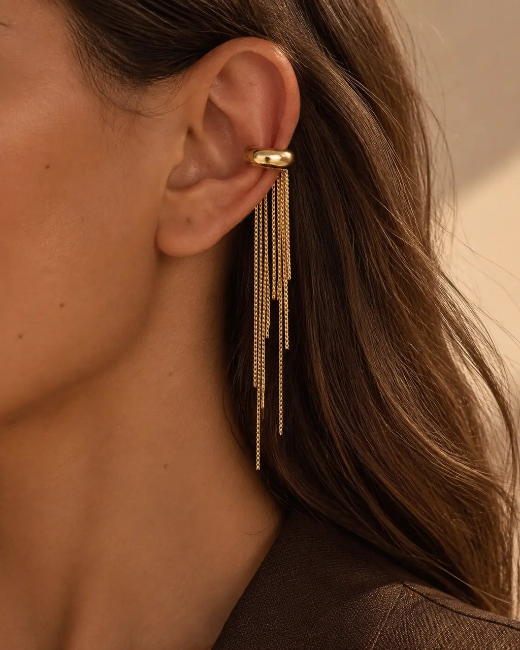 One gold-tone ear cuff with uneven chain fringes, close-up worn on the upper ear.