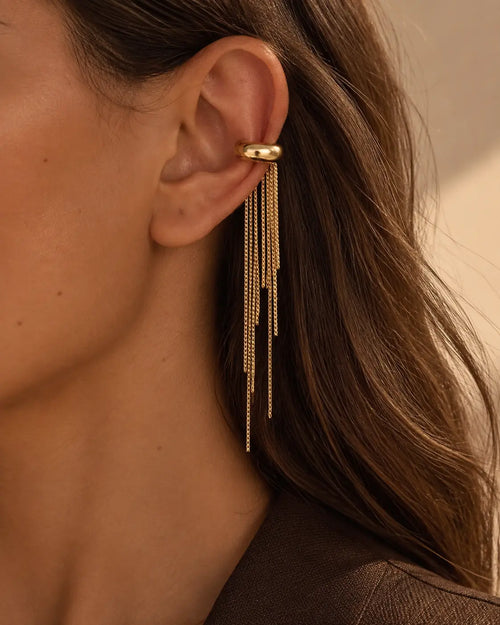 One gold-tone ear cuff with uneven chain fringes, close-up worn on the upper ear.