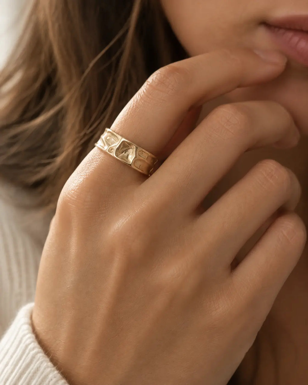 Gold-tone open band ring with a folded surface, close-up on a hand near the lips.
