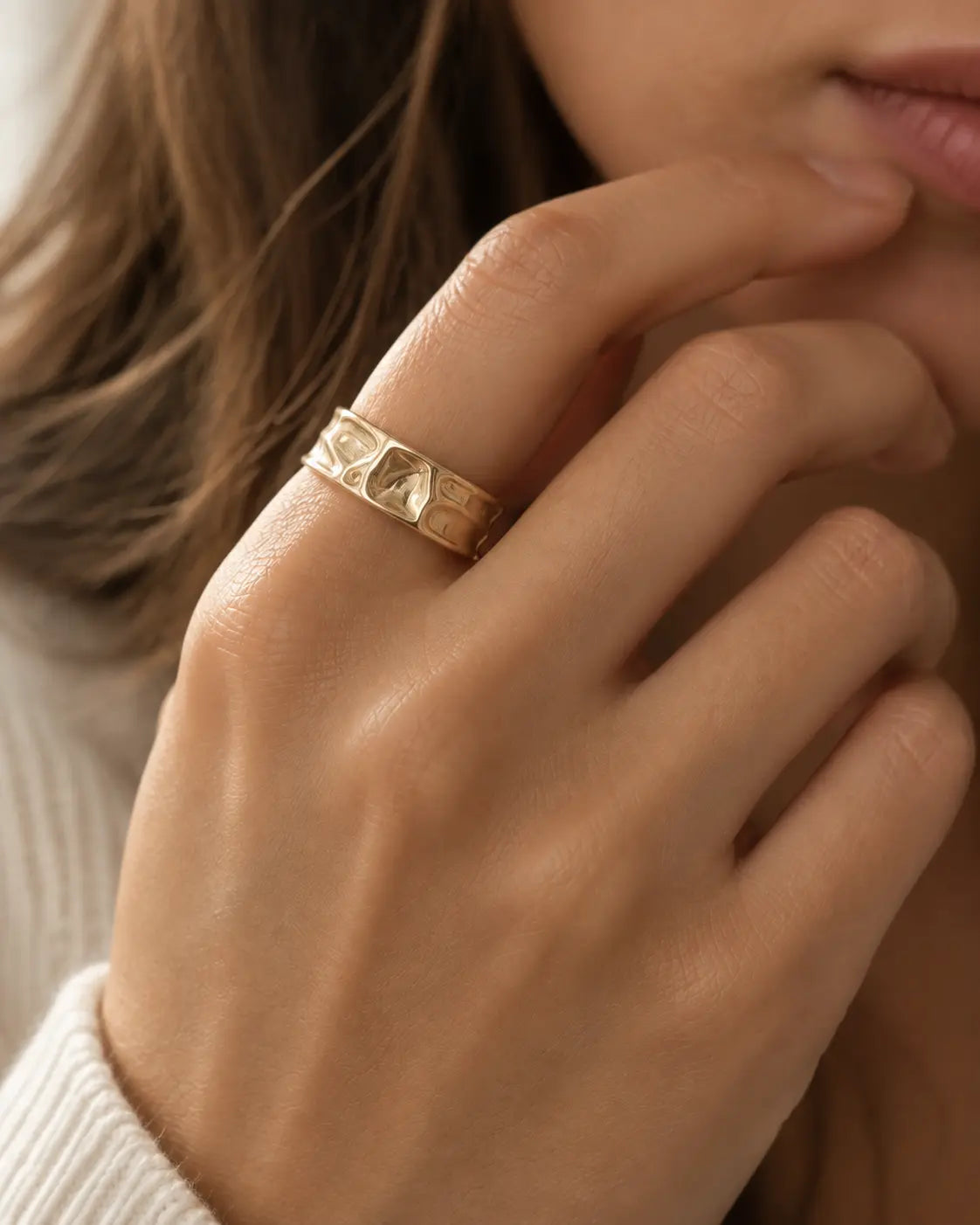 Gold-tone open band ring with a folded surface, close-up on a hand near the lips.