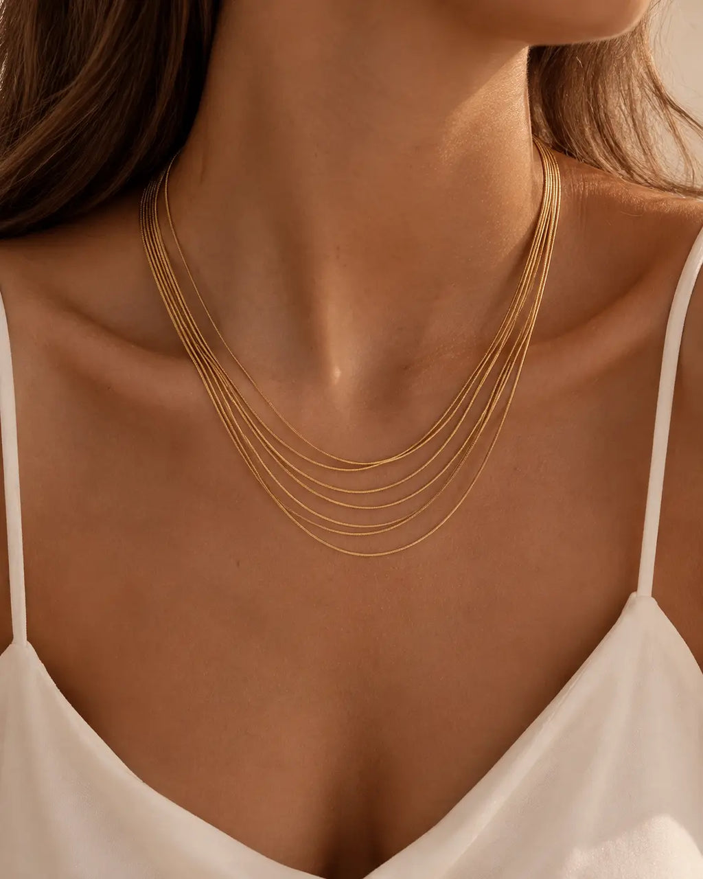 Gold-tone necklace with multiple fine chain strands in graduated lengths, worn at a V-shaped neckline.