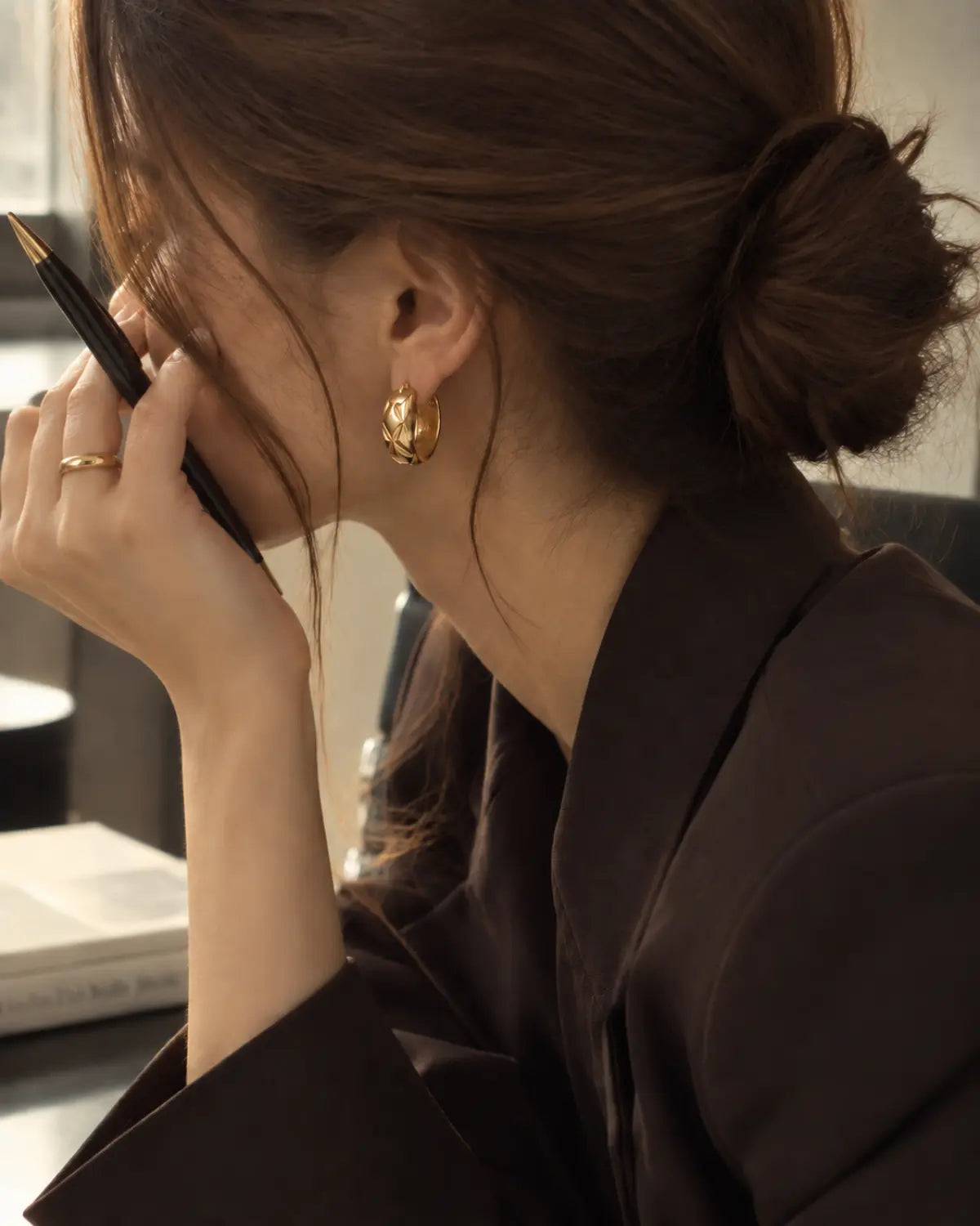 Quilted gold-tone huggie earring worn with hair tied back.