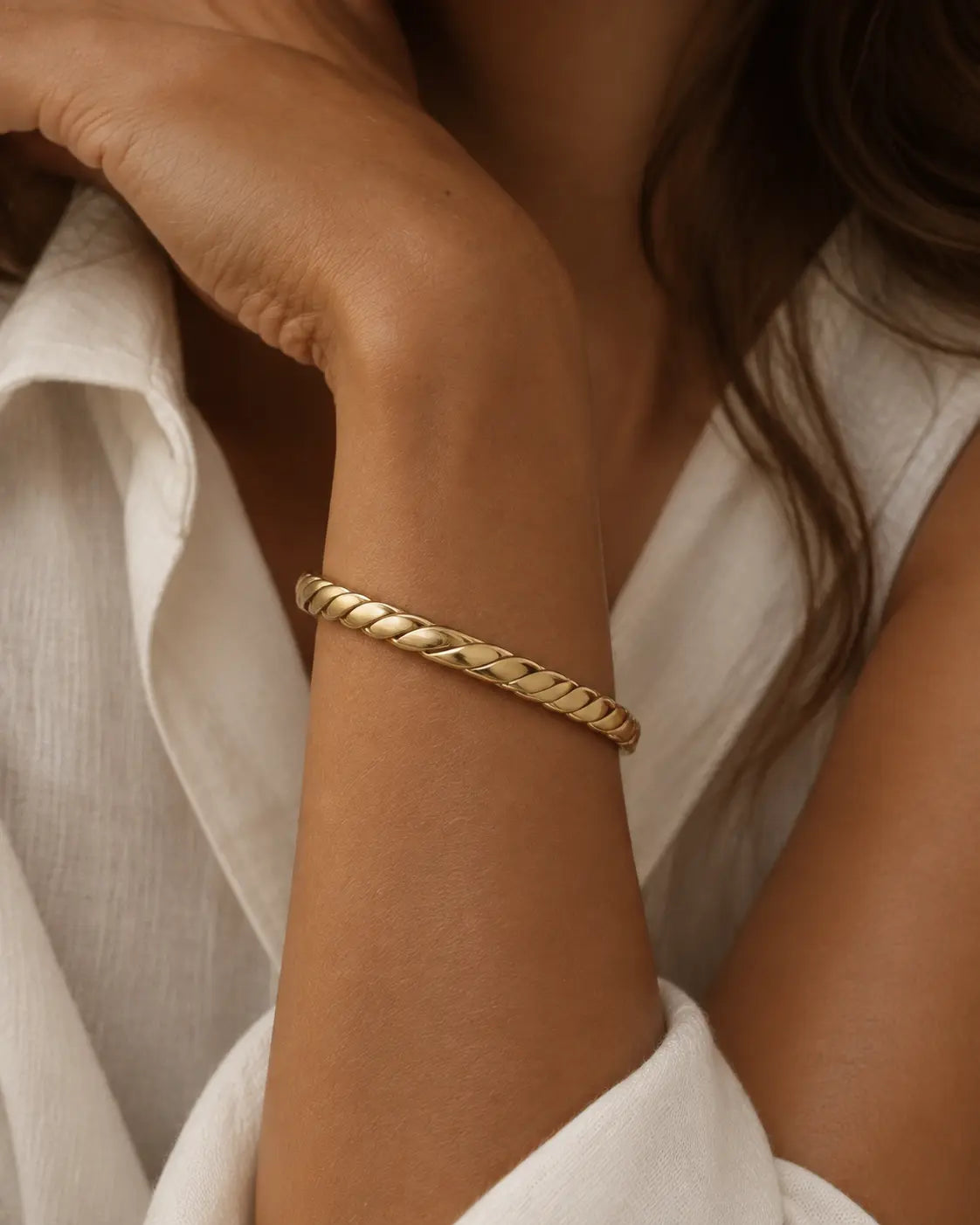 Gold-tone open bangle with a thick rope-twist pattern, close-up on a wrist near the chin.