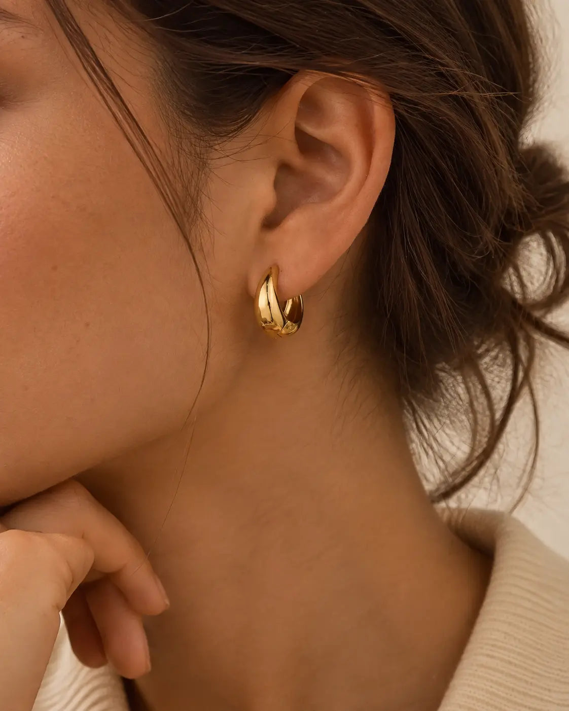 Close-up of a sculptural gold-tone teardrop hoop on the ear.