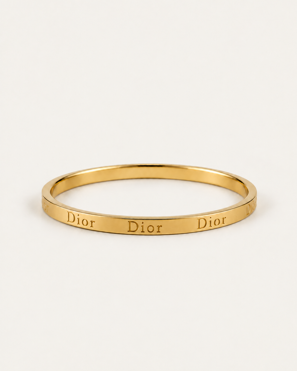 Gold-tone bangle with repeated engraved lettering, shown at an angle.