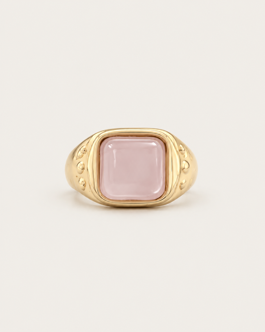 Gold-tone ring with a pale pink cushion-shaped accent, front view.