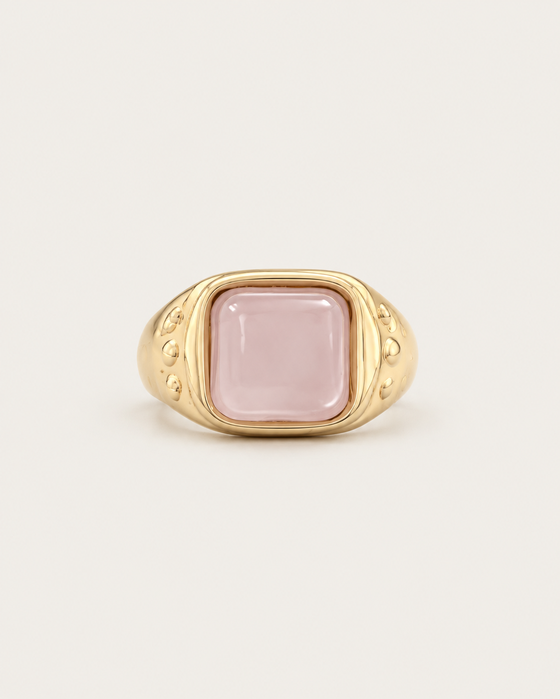 Gold-tone ring with a pale pink cushion-shaped accent, front view.