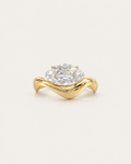 Gold-tone wave band ring with a raised clear stone accent, front view.