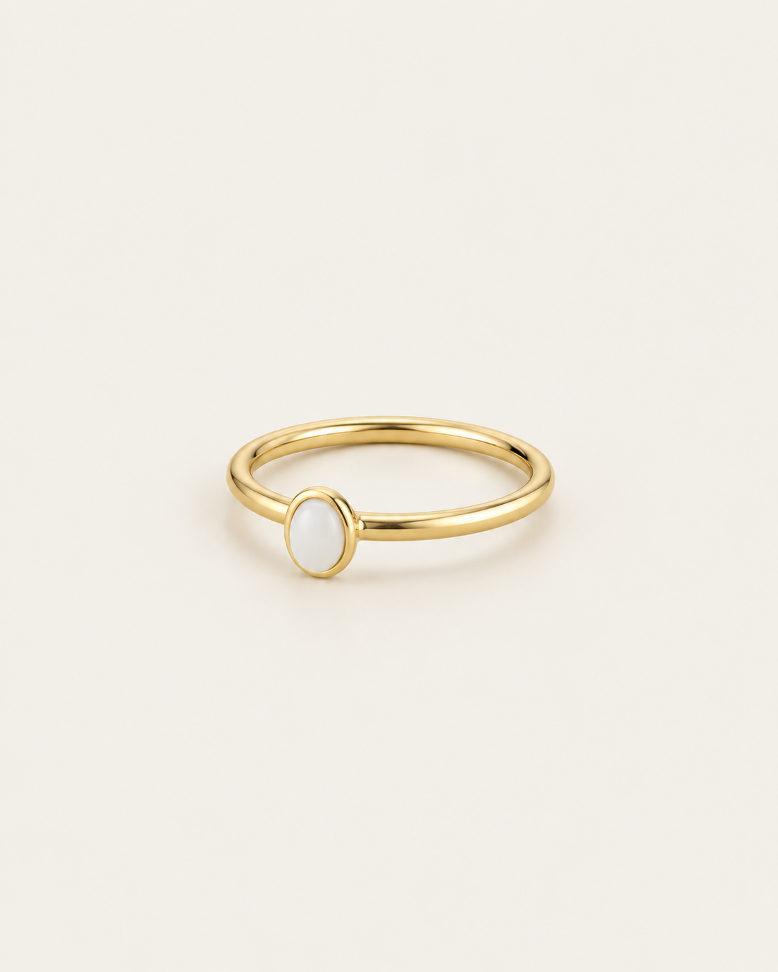Slim gold-tone ring with a white oval bezel accent, angled view of the narrow band.