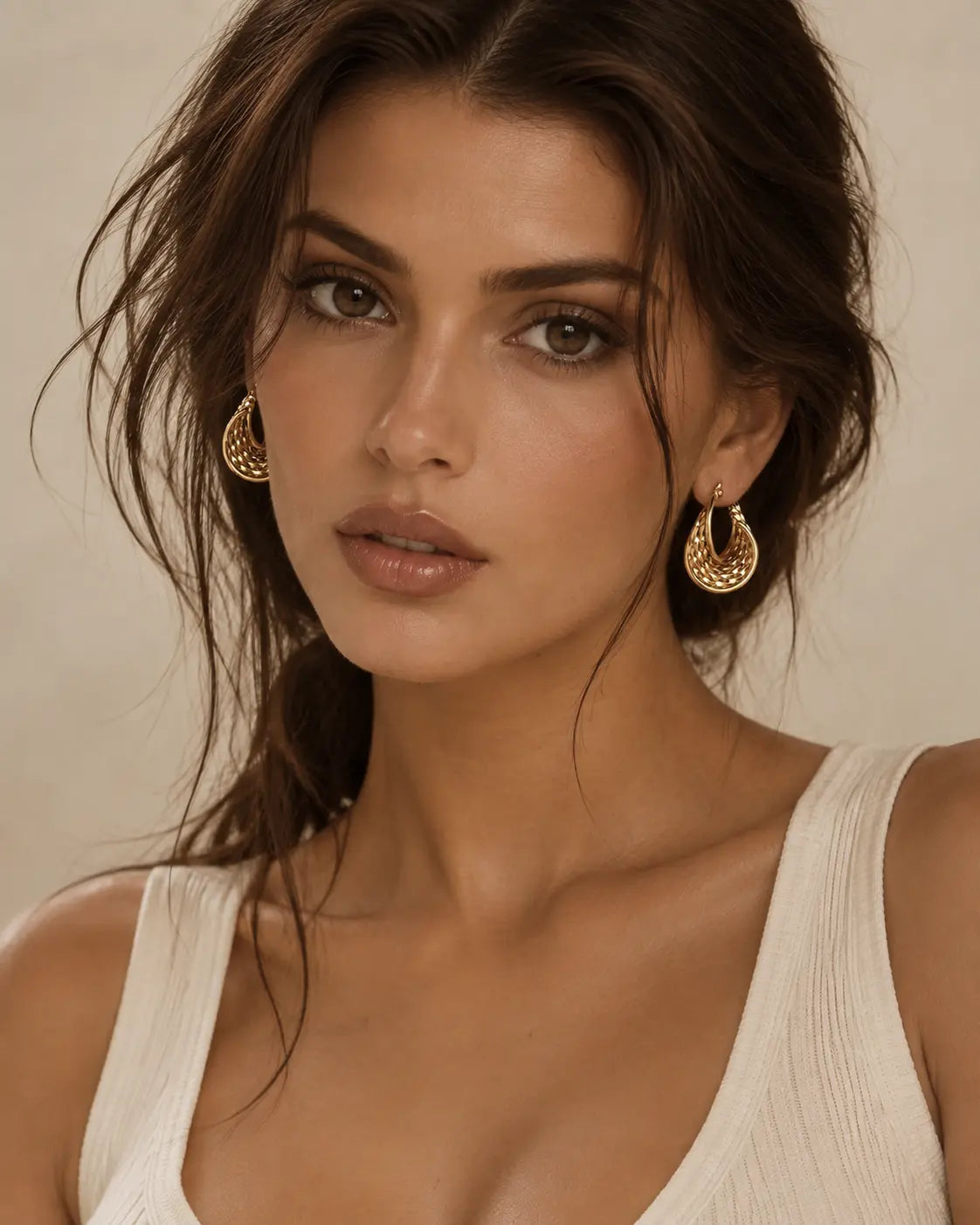 Woven gold-tone oval hoop earrings worn in a portrait.