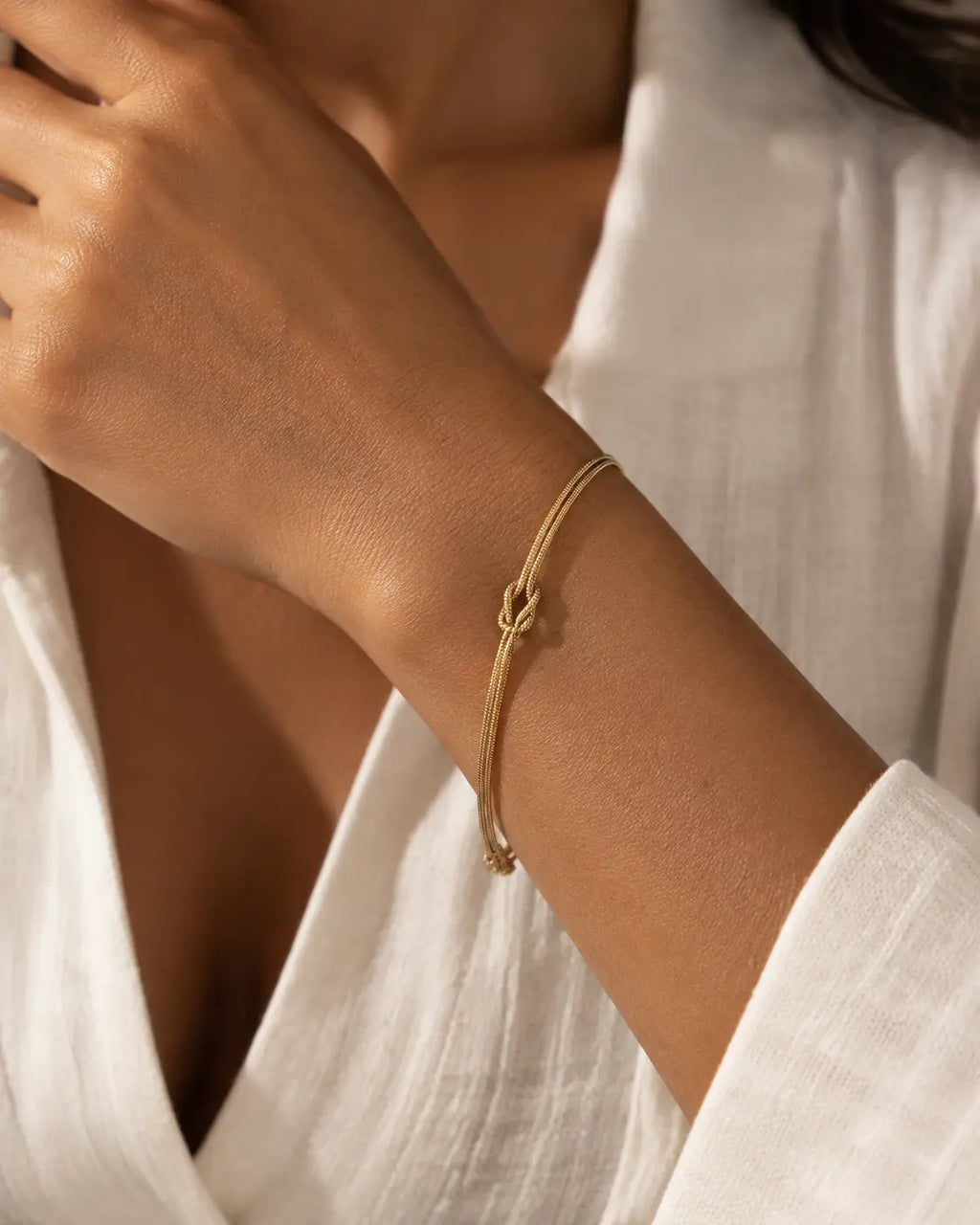 Gold-tone double-chain bracelet with a central knot, worn beside a white shirt cuff.