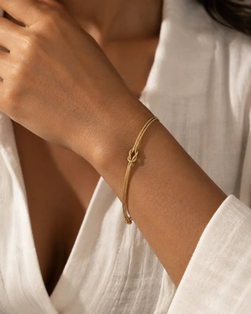 Gold-tone double-chain bracelet with a central knot, worn beside a white shirt cuff.
