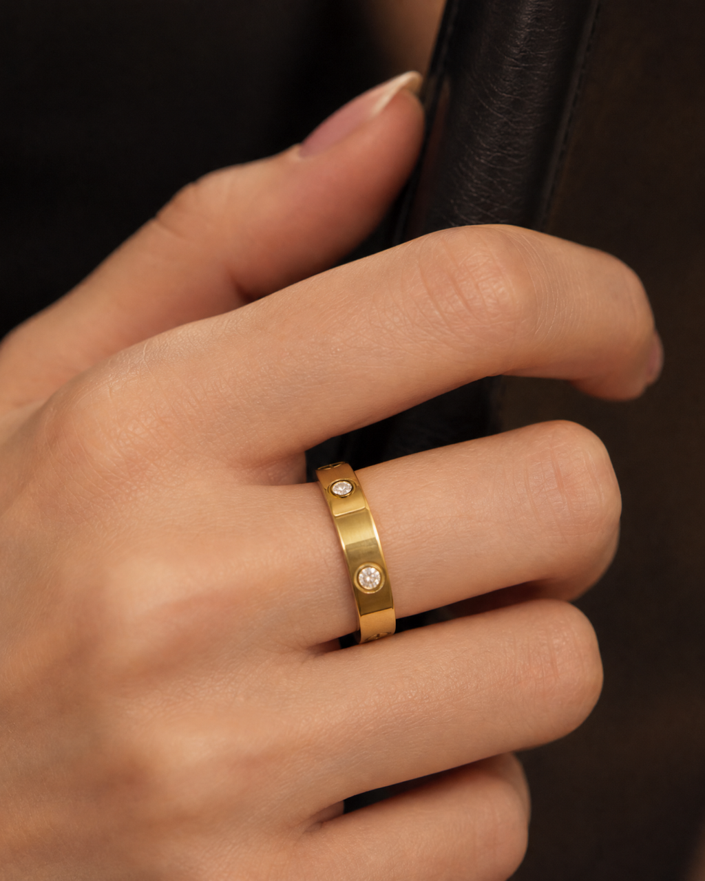 Gold-tone band ring with spaced round bezel-set stone accents, close-up of the ring against a black clutch.