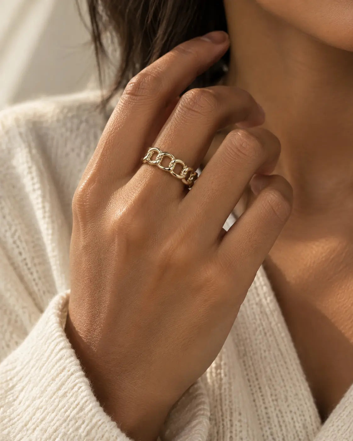 Gold-tone open ring with oval chain links, worn on a hand near the chin.