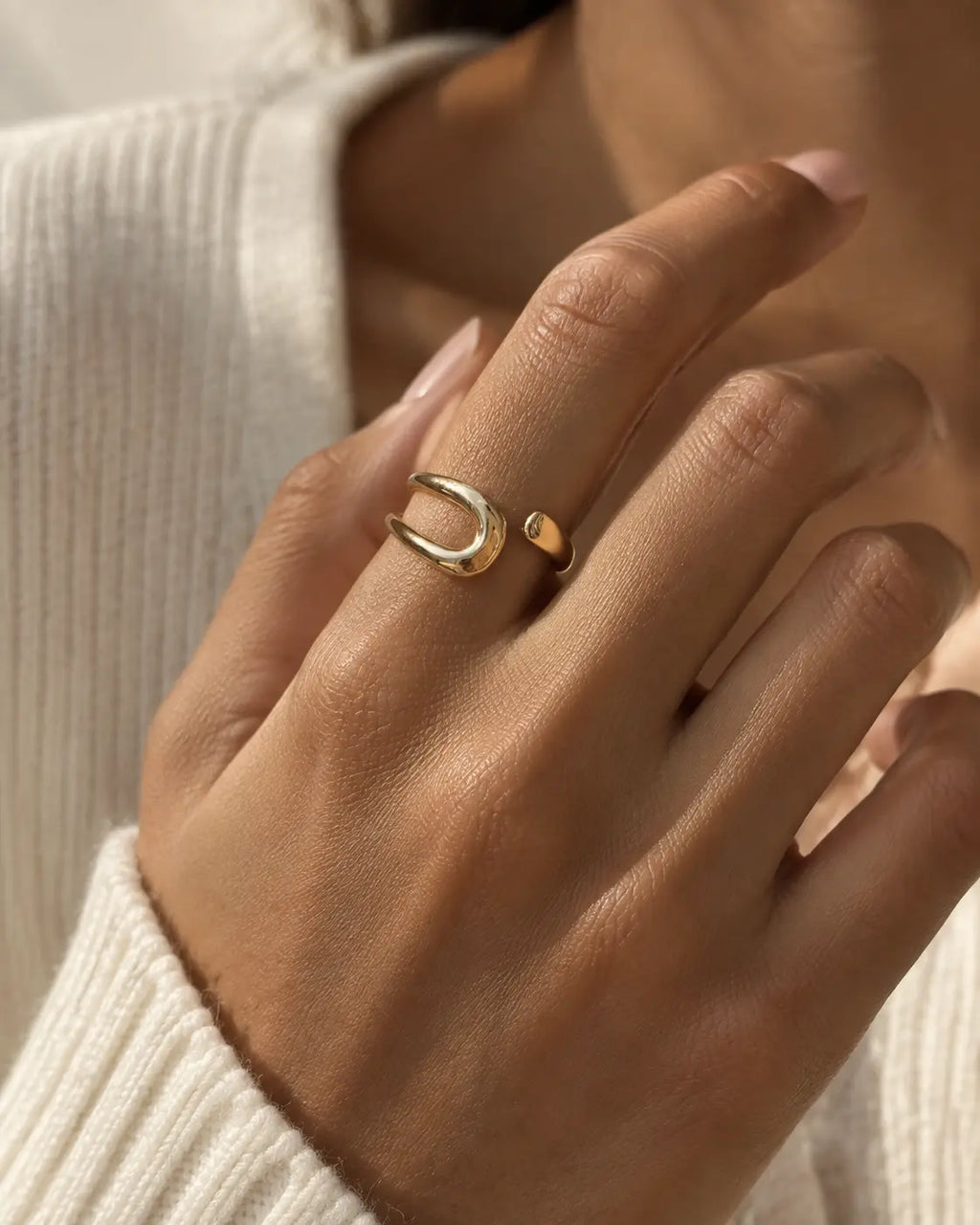 Gold-tone bypass ring with an open loop and tapered end, wider view on a raised hand.