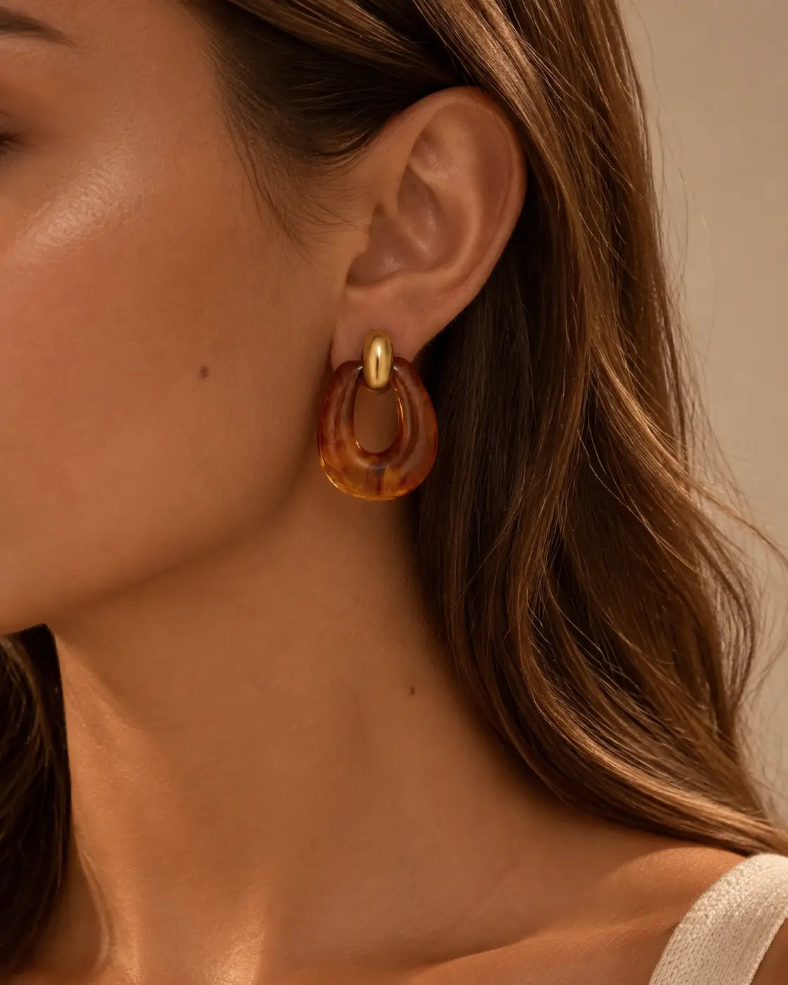 Close-up of a brown marbled oval drop earring on the ear.