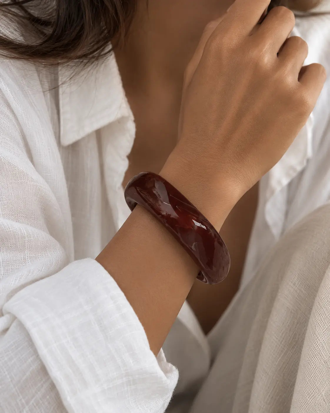 Chunky dark-brown bangle with an angular contour, worn on a wrist near the face.