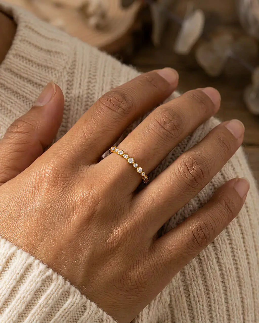 Gold-tone band ring with a row of clear stone accents, worn on a hand resting against cream knitwear.