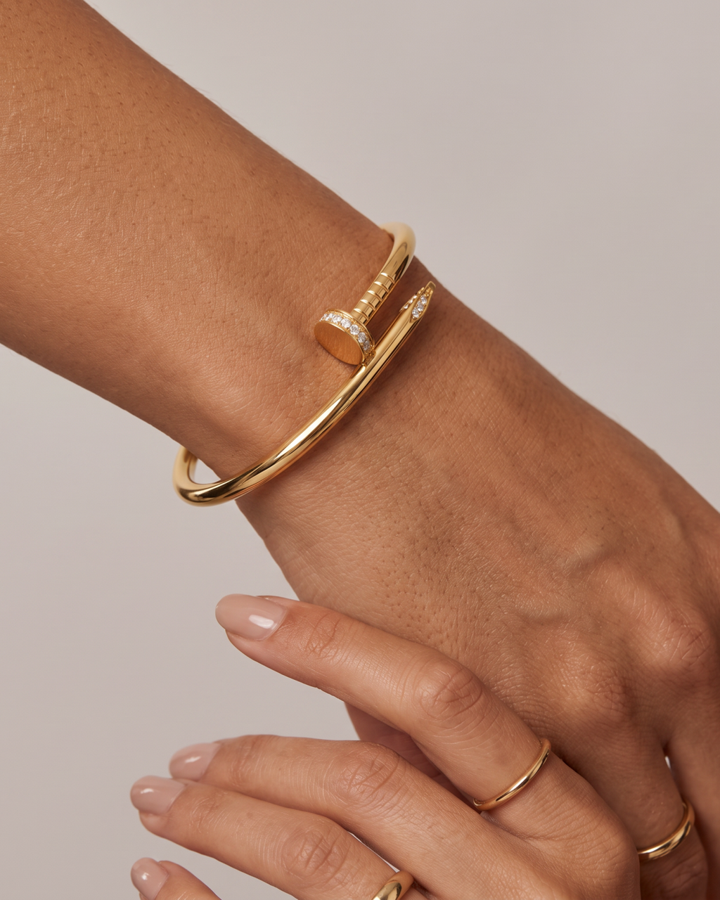 Gold-tone nail-shaped bangle with stone accents, worn on the wrist with the other hand nearby.