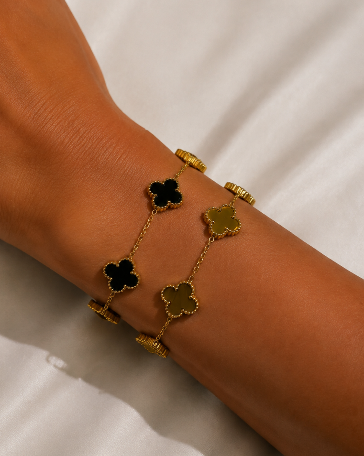 Dark-inlay and gold-tone clover bracelets worn together in a layered styling image.