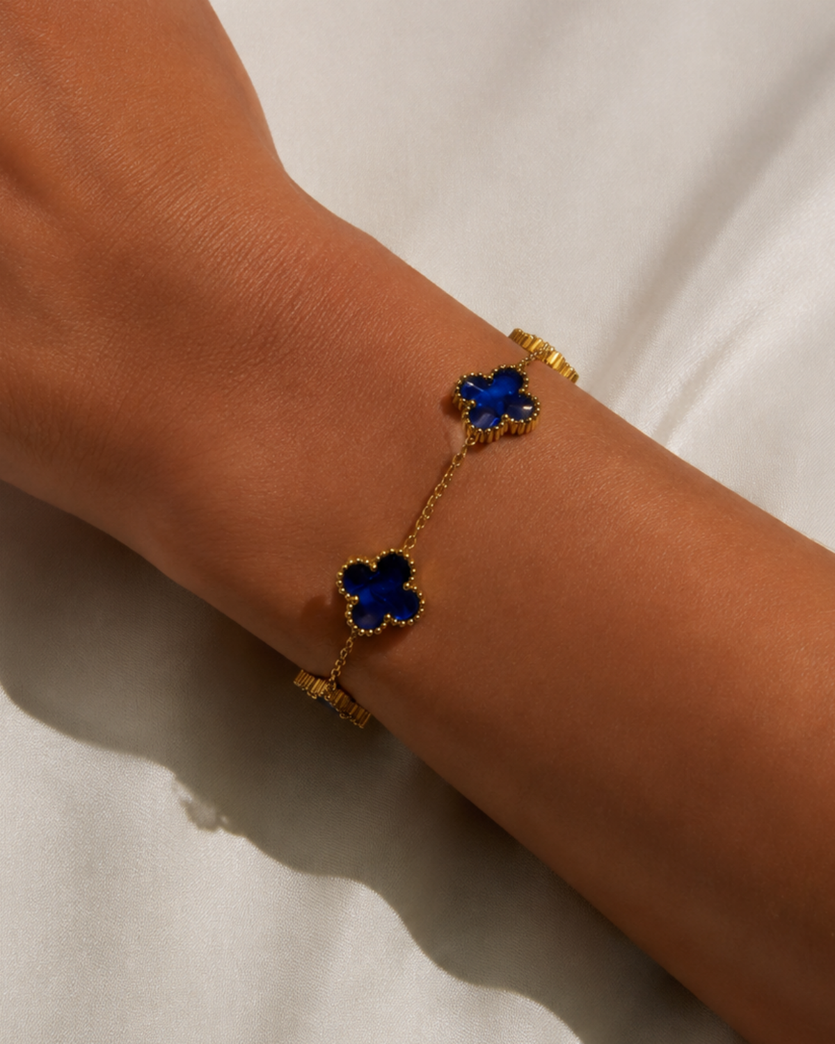 Chain bracelet with blue clover inlays worn across the wrist.