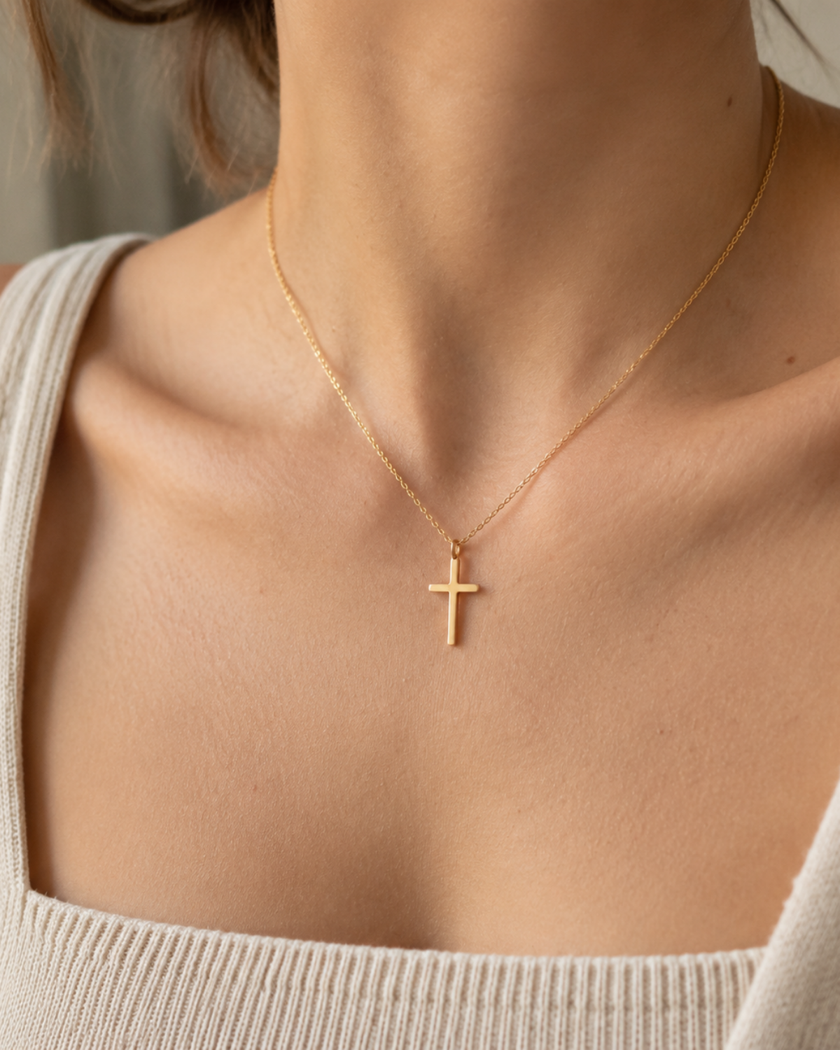 Gold-tone cross necklace worn at the neckline above a white ribbed top.